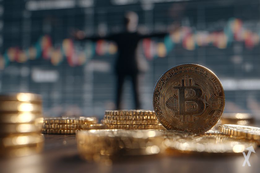 plusieurs coin bitcoin dorés et posés sur une table, au fond un trader heureux devant son graphique